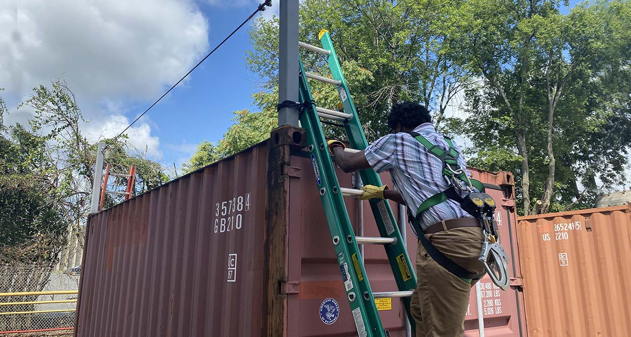 Man climbing a ladder against a shipping container to demonstrate fall protection methods